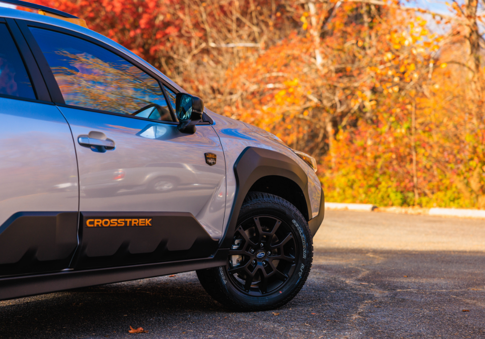 Close up of the passenger's side of anew Subaru Crosstrek with trees in the background